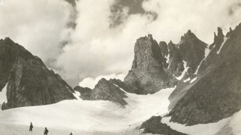 three climbers trudge through snow, surrounded by craggy peaks